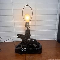 Black ceramic lamp with a sculpted leopard figure on a base, lamp turned on with a warm filament bulb.