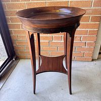 Front view of vintage wooden table showing round top with rim, slender round saber legs, and curved lower shelf.