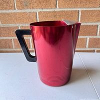 Front side view showing red aluminum pitcher with black handle.
