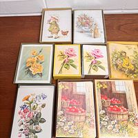 Top-down photo showing nine vintage note card sets including framed and boxed flower and child illustrations in pastel colors.