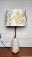 Front view of the lamp showing full height, ceramic base, wooden neck, and the felt pattern lampshade with floral designs.