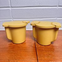 Two mustard yellow plastic containers with lids assembled, the cream pitcher on the left and sugar bowl on the right, shown side by side.
