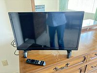 Front view of Insignia 24" LED TV and remote placed on wooden dresser.
