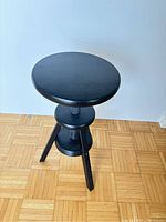 Front and top view of the black adjustable bar stool showing the round seat and screw mechanism.