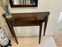 Front view of the dark wooden Bombay console entry table with drawer and decorative round pulls under a mirror.
