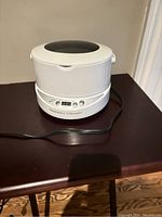 Front view of white Hammacher Schlemmer digital ultrasonic cleaner placed on a wooden surface, showing display panel and control buttons.