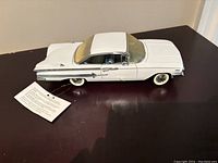 White 1960 Chevrolet Impala model car displayed on table, showing side view with details and attached tag.