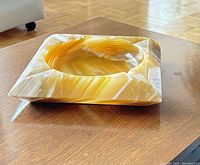 Angled close-up side view of honey onyx marble ashtray showing smooth polished surface and shape