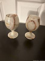 Two beige and orange onyx marble wine goblets standing upright, showing natural veining and shape.