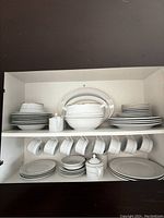 View of the full set in a cabinet showing stacked plates, bowls, cups hung on rack, sugar bowl, and serving pieces with visible gold trim.