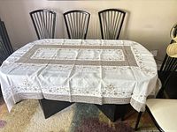 Large white vintage tablecloth with Madeira cutwork and embroidery spread over a dining table, showing embroidered floral designs and detailed cutwork patterns along the edges and center area.