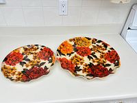 Two round trays with mid century floral fabric design under plexiglass-like material, showing orange, red and yellow flowers with green leaves. Scalloped edges visible.