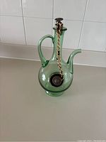 Green translucent glass wine decanter/carafe with an integrated ice chamber, handle, spout, and metal stoppers attached by gold-toned chain