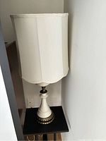 Side view of one ceramic table lamp with cream scalloped fabric shade on a small black table.