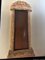 Front view of the wall fountain showing rectangular glass panel framed by decorative faux stone frame with a curved top and bottom.