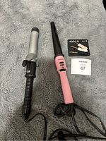 Photo showing two curling tools on grey fabric, a silver Conair curling iron and pink curling wand with tapered barrel and buttons on handle.