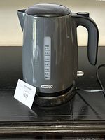 Front view of gray Dash electric kettle showing water level indicator and handle with power cord on black base.