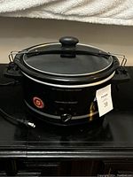 Front view of Hamilton Beach slow cooker showing glass lid, black body, control knob, and 5 year warranty sticker.