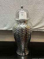 Front view of a large ginger jar with a chrome hammered finish and a domed lid with a finial knob
