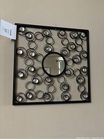 Full view of one metal wall art piece showing square frame, central mirror and surrounding metal loops with crystals.
