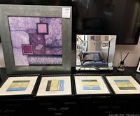 Image showing one large framed purple abstract art with greenish frame, four small framed prints with modern designs in white frames, and one square beveled mirror on a dark surface.