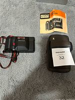 Pentax PC 35 AF DATE 35mm camera with instruction manual and carrying case displayed on gray fabric surface.