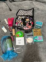 Full view of all makeup and beauty products laid out on fabric surface including a striped cosmetic bag.