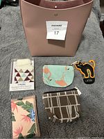 Image showing pink plastic purse, black cat holder, two change pouches, Kleenex, and hand warmer.