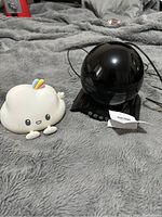 Two light items on gray fabric surface: black starry night light projector and white cloud silicone night light with rainbow decoration