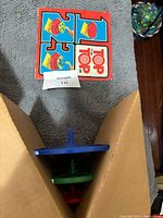 Top viewed standing upright next to instruction sheet showing colorful top images and logo.