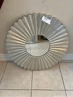 Full view of the round wall mirror with a fluted metallic frame and visible wear marks.