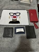Photo showing five wallets and a white clutch bag with a face design, red women's wallet with tassel, and black wallets