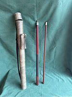 Two-piece red pool cue sections positioned beside grey cylindrical case