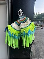 Two handmade dance hackle bustles featuring rainbow-colored beadwork, neon green, yellow, and blue feathers, and neon green fringe strips, hanging together showing vibrant colors and design details.