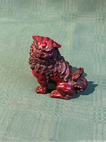 Red cinnabar resin Fu Guardian Lion Foo Dog statue showing front and side view highlighting the detailed mane, facial features, and curved tail.