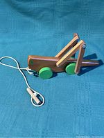 Photo showing side view of wooden pull toy shaped like a grasshopper with green wheels and attached pull string with wooden handle.