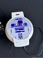 Waffle maker closed showing top with R2-D2 design and power cord to the right.