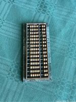 Top view photo of vintage brass abacus on green marble base, showing brass beads and rods in aligned rows.