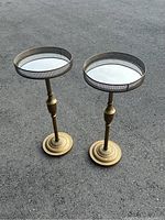 Pair of vintage brass flower stands with round mirrored tops and perforated brass rims, shown on pavement surface