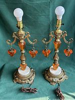 Pair of vintage bronze and amber glass table lamps with marble bases and decorative hanging amber glass pendants displayed together against green fabric background.