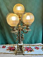Front view of vintage brass and marble table lamp with four ribbed glass globes lit, showing ornate base and cherub accents.