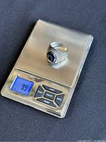 Top view of vintage silver ring with black stone on digital scale weighing 9.91 grams.