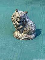 Front and slightly angled view of the small metal lion figurine showing detailed mane and face, resting on a textured base.