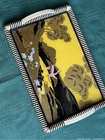 Photo showing the top side of the vintage serving tray with painted bird and floral design on yellow background, featuring black and white woven border.