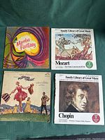 Four vinyl records with covers: Mambo Fantasy, The Sound of Music, Mozart piano concerto, and Chopin composer portrait. Arranged on green fabric background.
