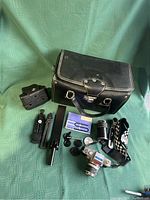 Full lot overview showing camera, lens, carrying case, accessory case, two tripods, strap and other items on green fabric background.