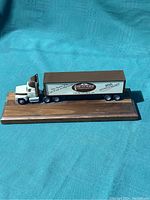 Top side view of the white and gray die cast semi-truck and trailer with 30th anniversary Smuckers Harness Shop branding, displayed on a wooden base.
