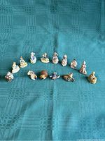 Fourteen small, hand-painted ceramic figurines arranged on a green cloth, including human characters in vintage attire and animals.