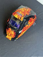 Front angled view of the black welding helmet with flame decals and auto-darkening lens.