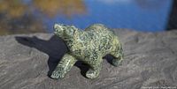 Front angled view of the green soapstone polar bear carving placed on a rock surface in natural light.